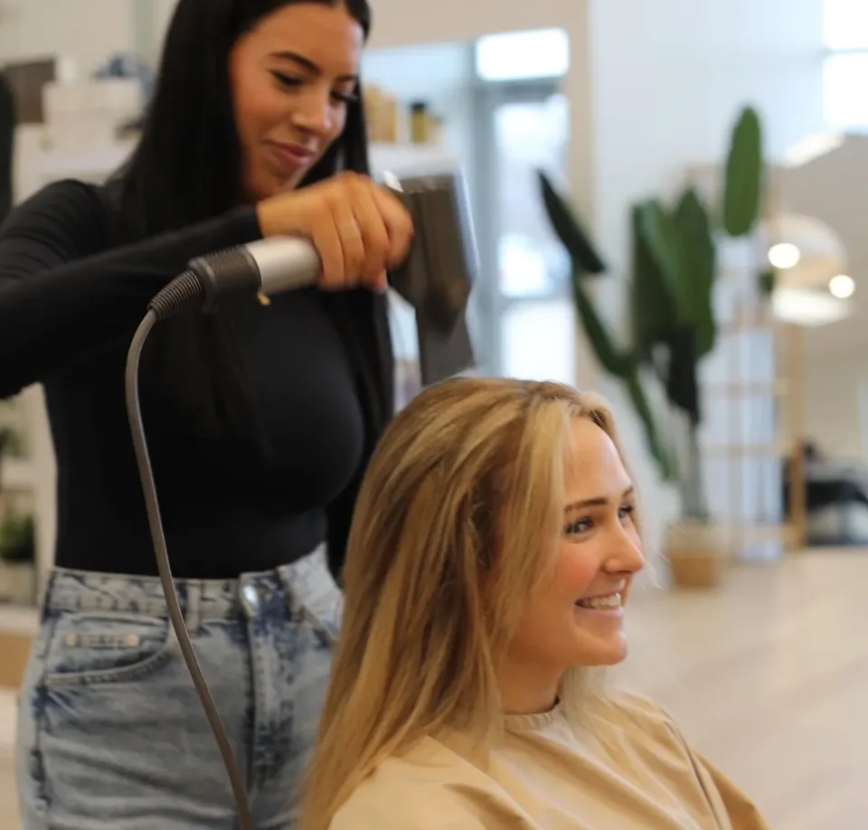 A Salon Elite stylist blow-drying a smiling client's hair in the bright studio